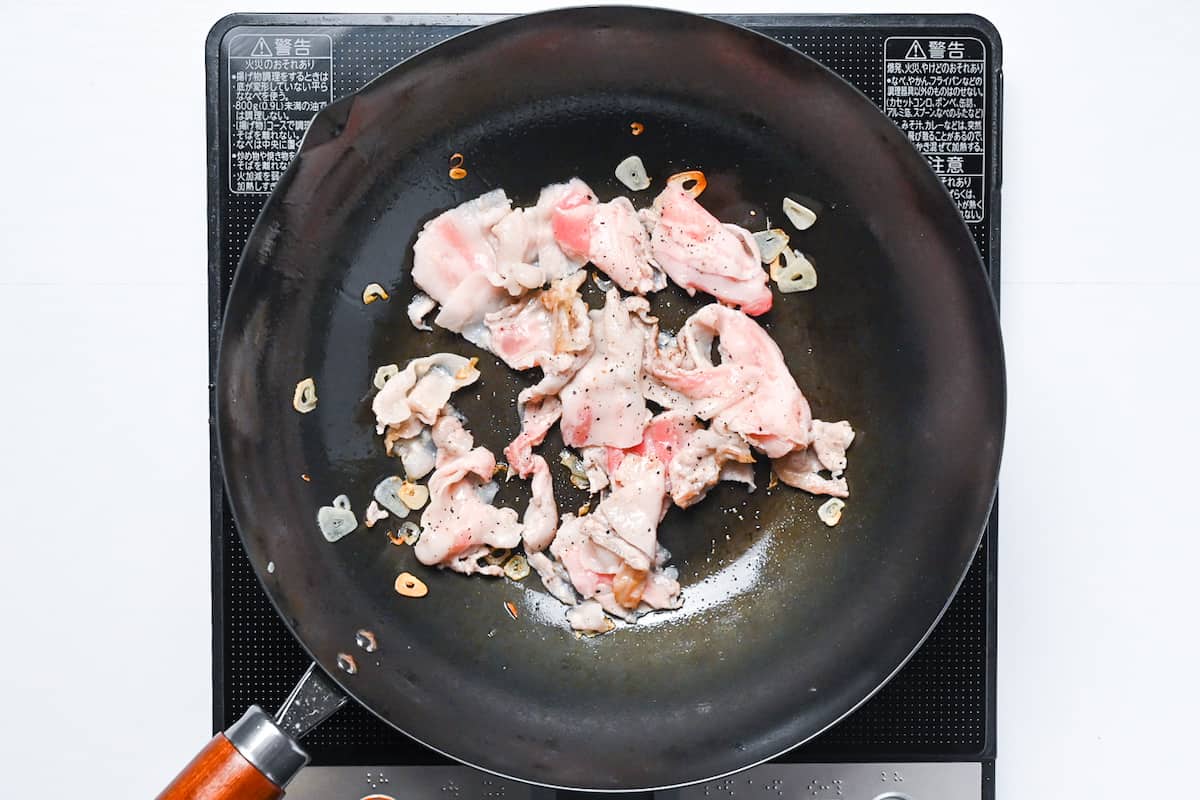 thinly sliced pork frying in a wok