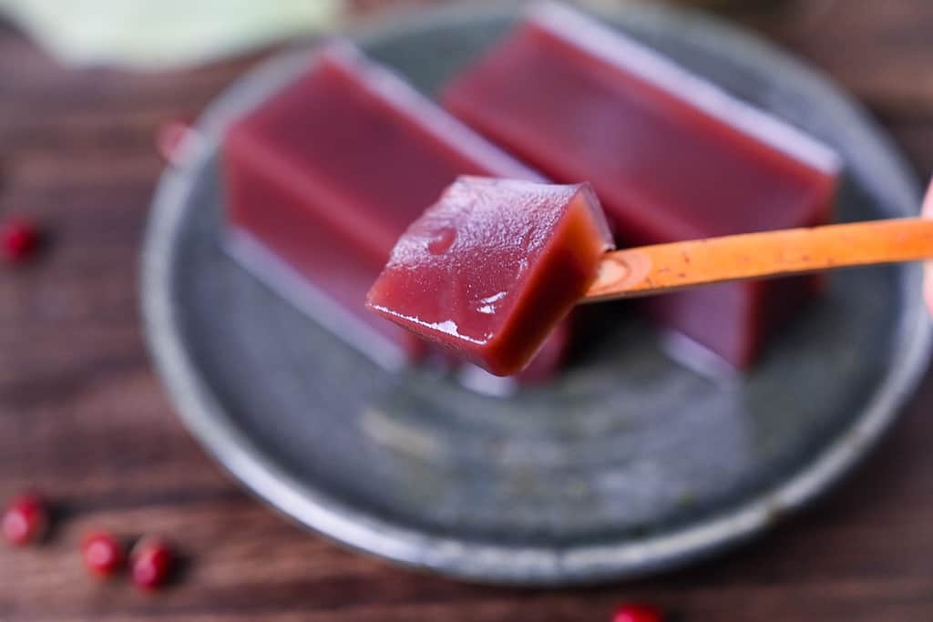 Two slices of mizu yokan red bean jelly on a green plate with green tea