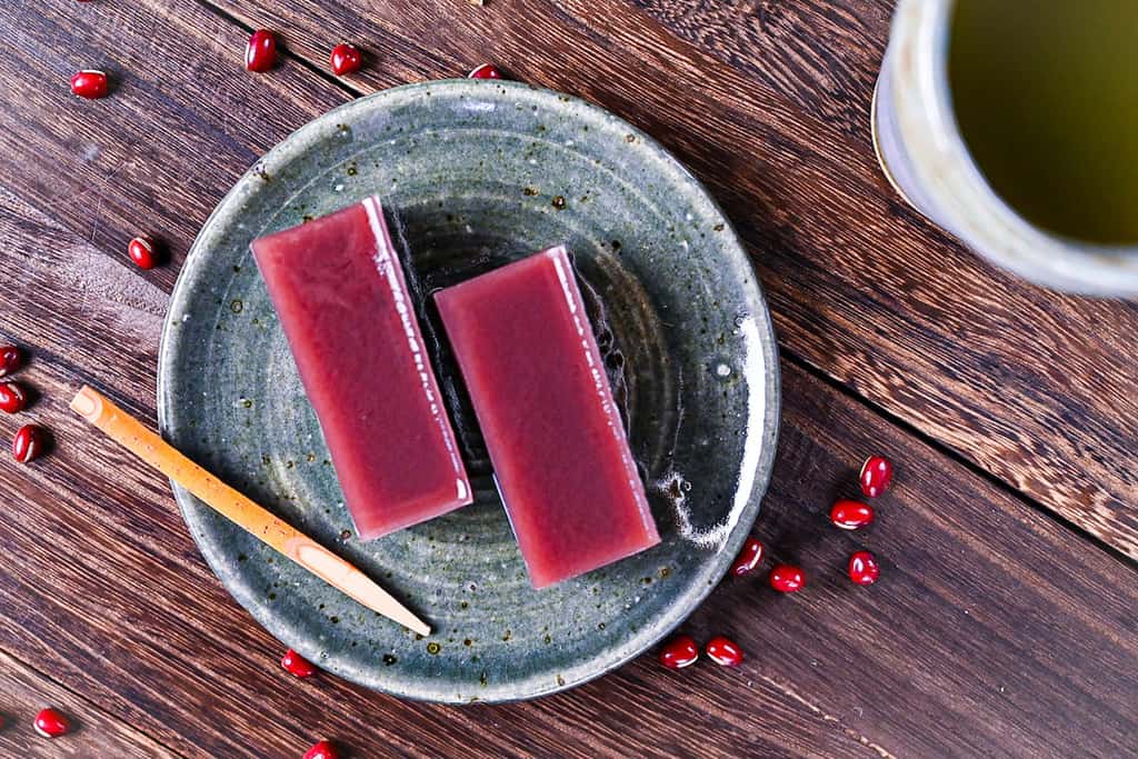 Two slices of mizu yokan red bean jelly on a green plate with green tea