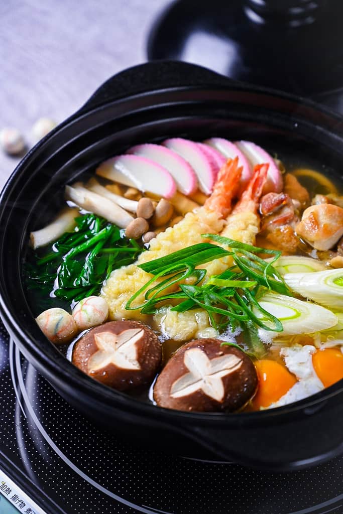 Nabeyaki Udon in a black donabe with chicken, shrimp tempura and vegetables