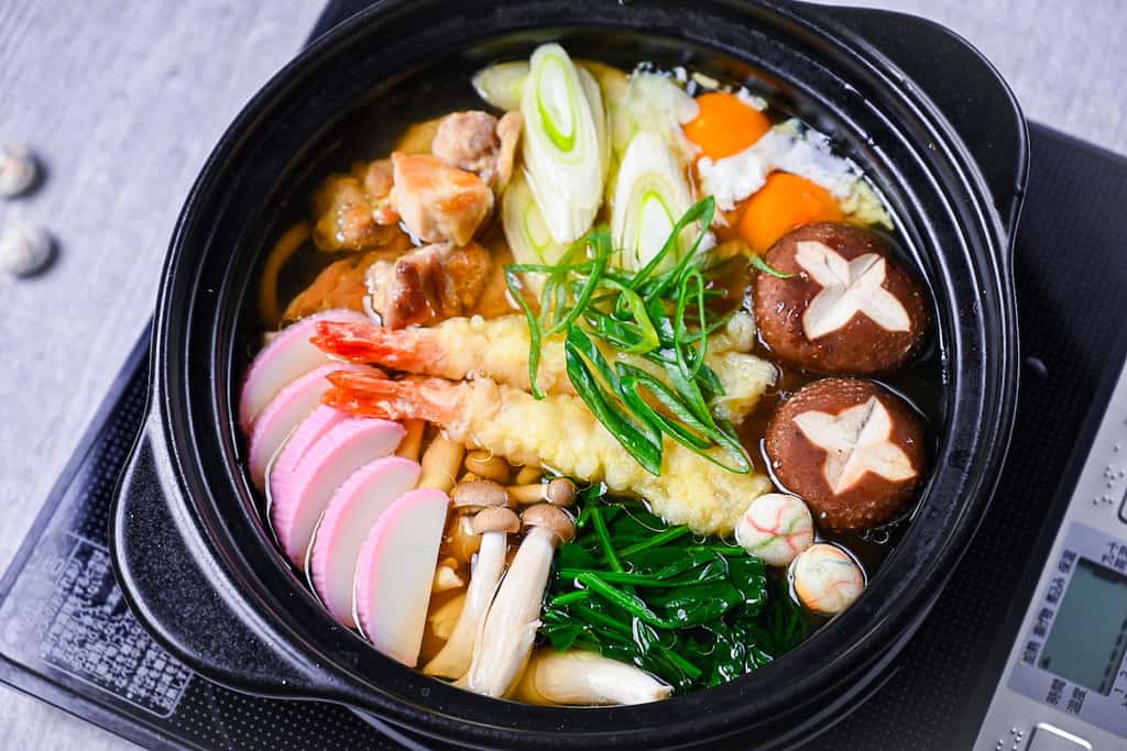 Nabeyaki Udon in a black donabe with chicken, shrimp tempura and vegetables