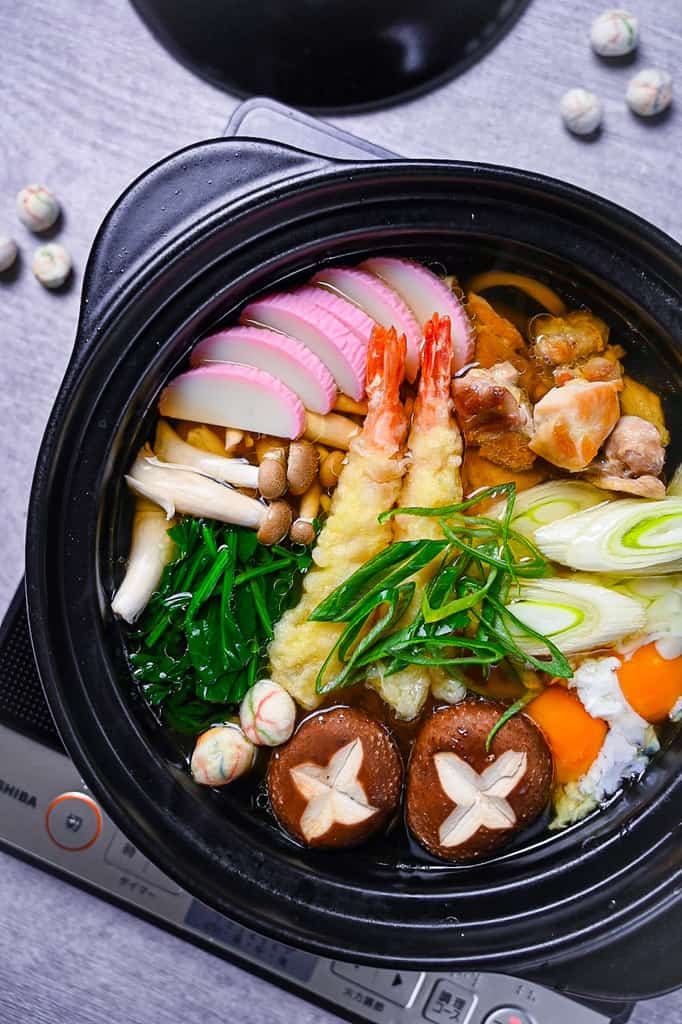 Nabeyaki Udon in a black donabe with chicken, shrimp tempura and vegetables