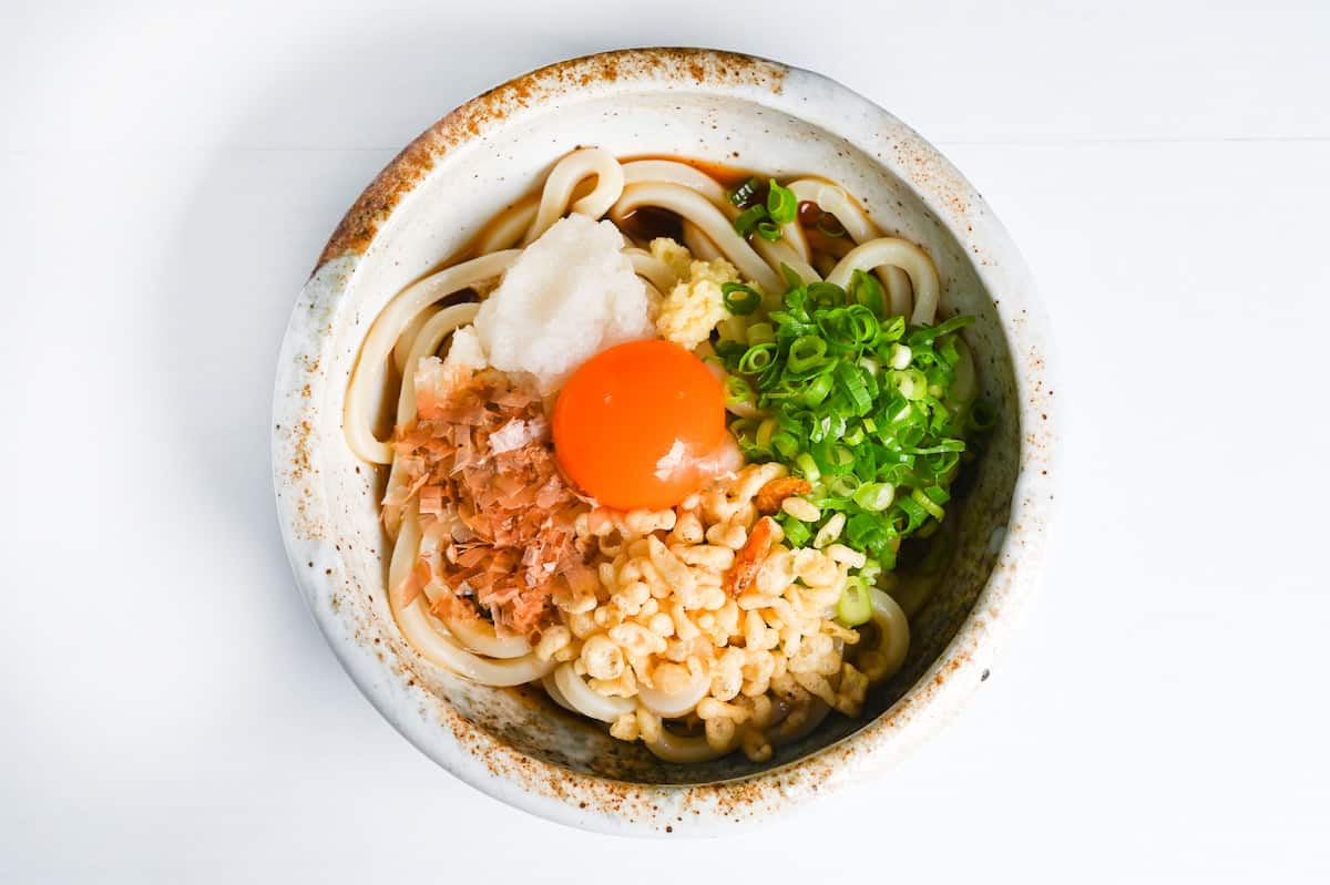 Bukkake udon topped with egg yolk, chopped green onion, grated daikon, tempura bits and bonito flakes