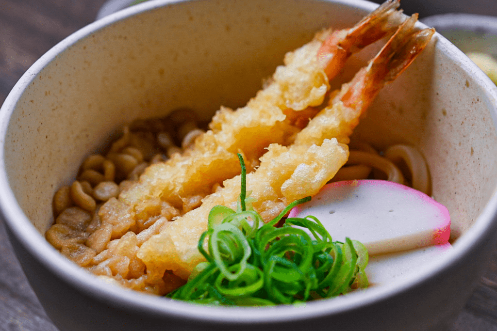 Ebiten udon served in a cream bowl with spring onion, grated ginger and pickles on the side