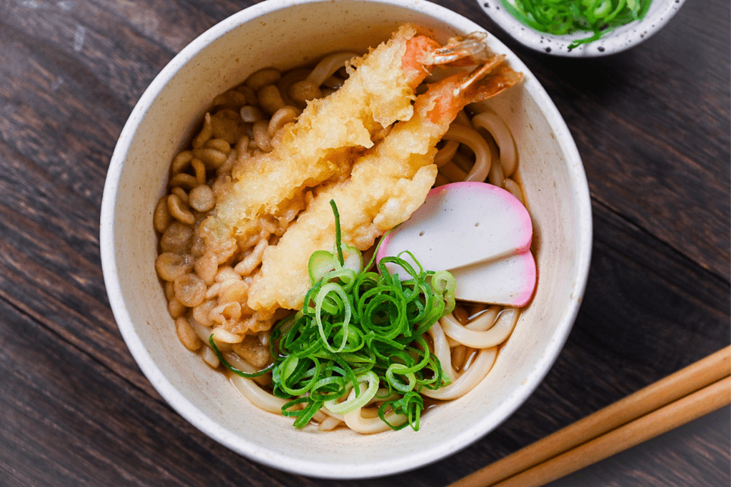 Ebiten udon served in a cream bowl with spring onion, grated ginger and pickles on the side top down