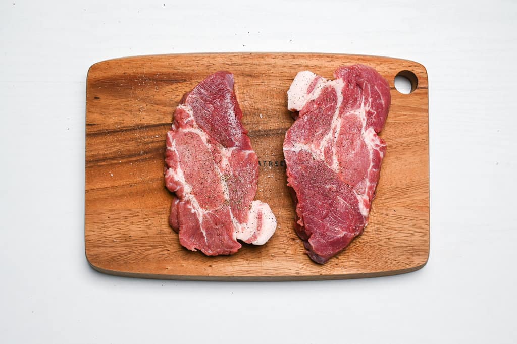 two pork chops on a wooden chopping board