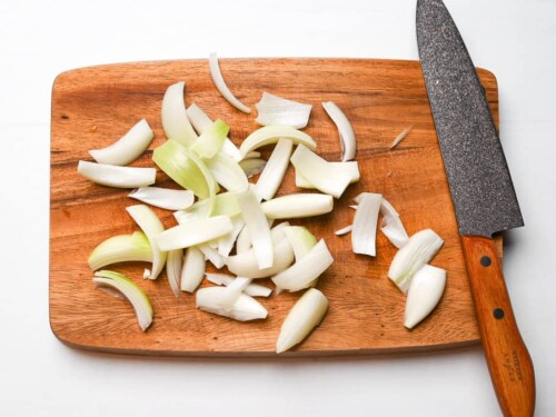 Cut onion wedges on wooden chopping board with knife