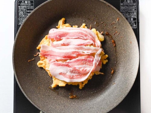 adding strips of thinly sliced pork belly to okonomiyaki