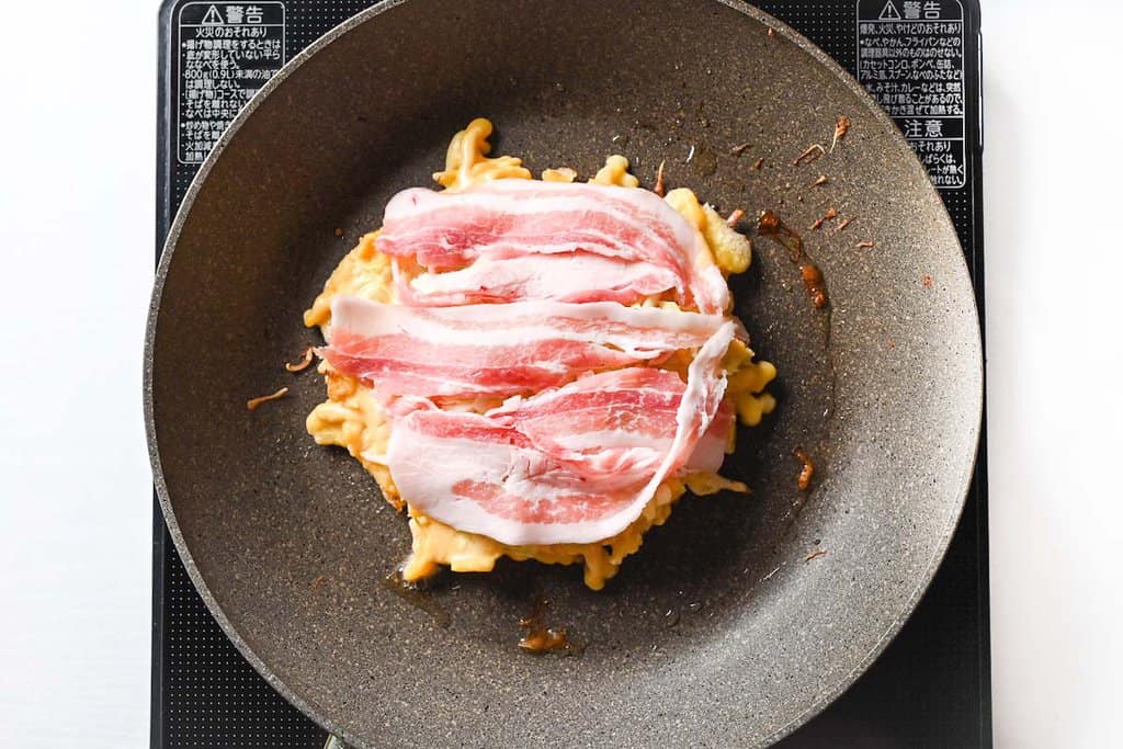 adding strips of thinly sliced pork belly to okonomiyaki