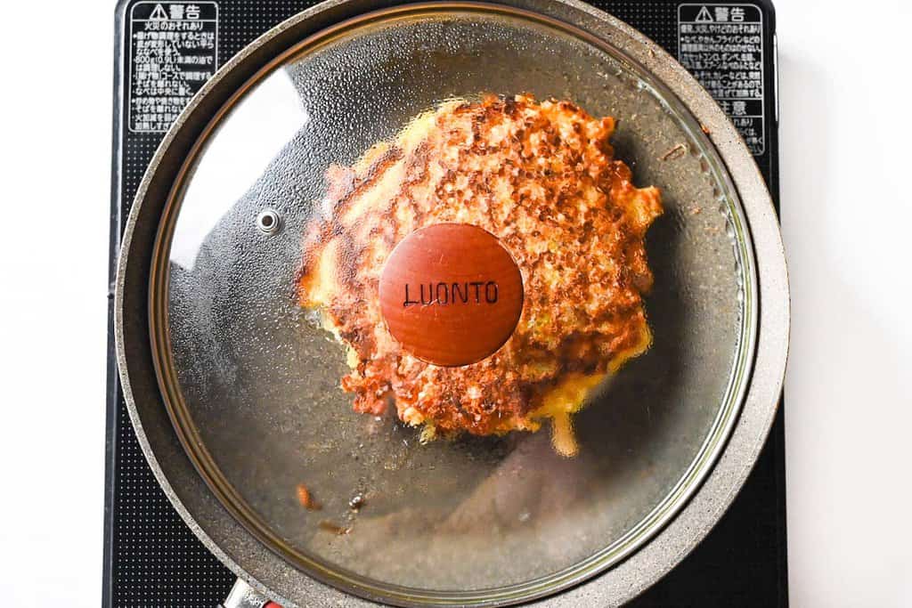 cooking okonomiyaki in a pan with the lid on