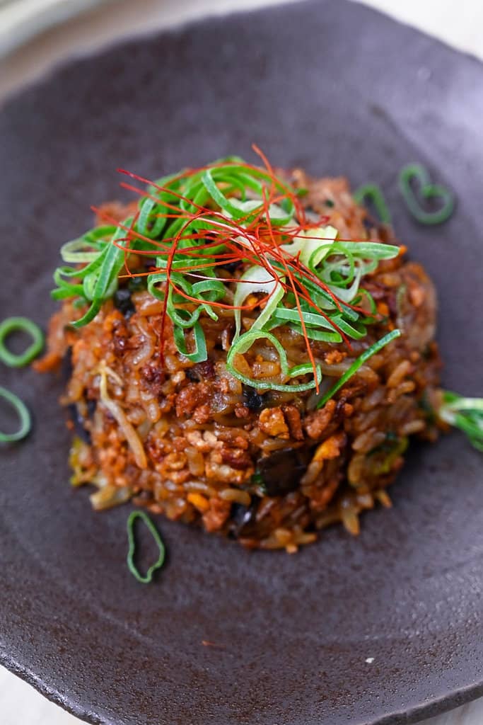 Pork and miso yakimeshi (Japanese fried rice) on a brown plate sprinkled with chopped spring onions and chilli threads