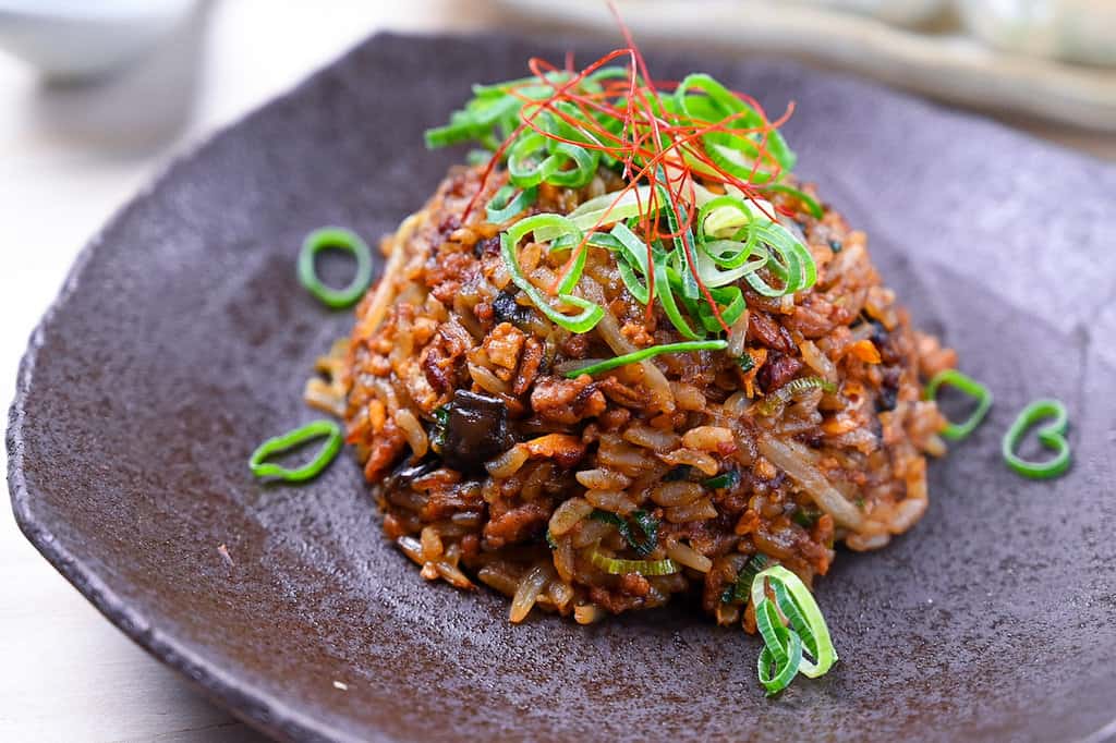 Pork and miso yakimeshi (Japanese fried rice) on a brown plate sprinkled with chopped spring onions and chilli threads