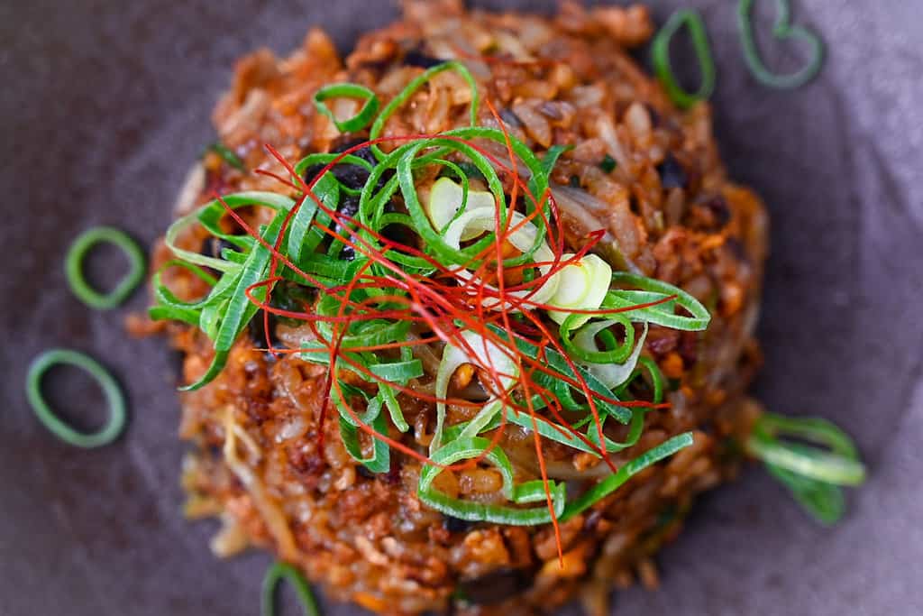 Pork and miso yakimeshi (Japanese fried rice) on a brown plate sprinkled with chopped spring onions and chilli threads