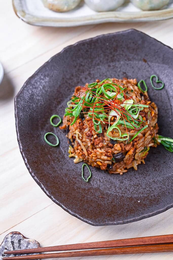 Pork and miso yakimeshi (Japanese fried rice) on a brown plate sprinkled with chopped spring onions and chilli threads