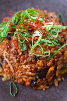 Pork and miso yakimeshi (Japanese fried rice) on a brown plate sprinkled with chopped spring onions and chilli threads