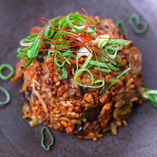 Pork and miso yakimeshi (Japanese fried rice) on a brown plate sprinkled with chopped spring onions and chilli threads