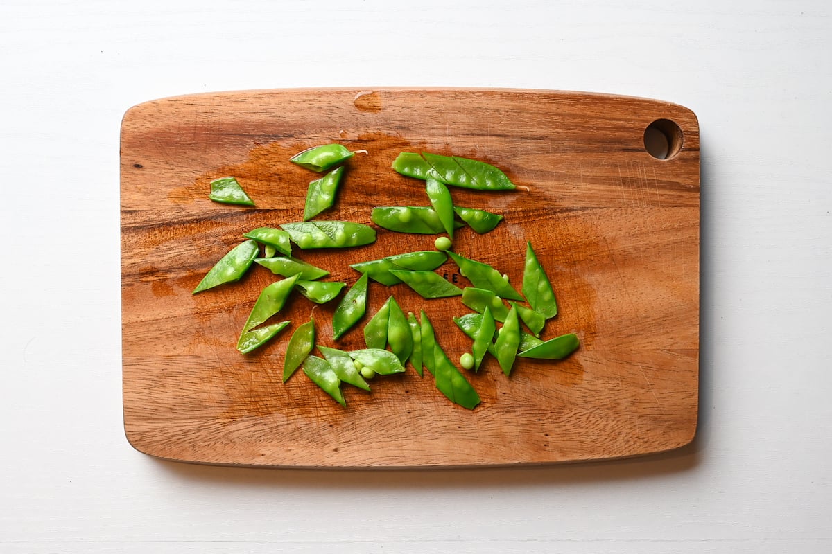 Nikujaga: cutting snowpeas on wooden chopping board