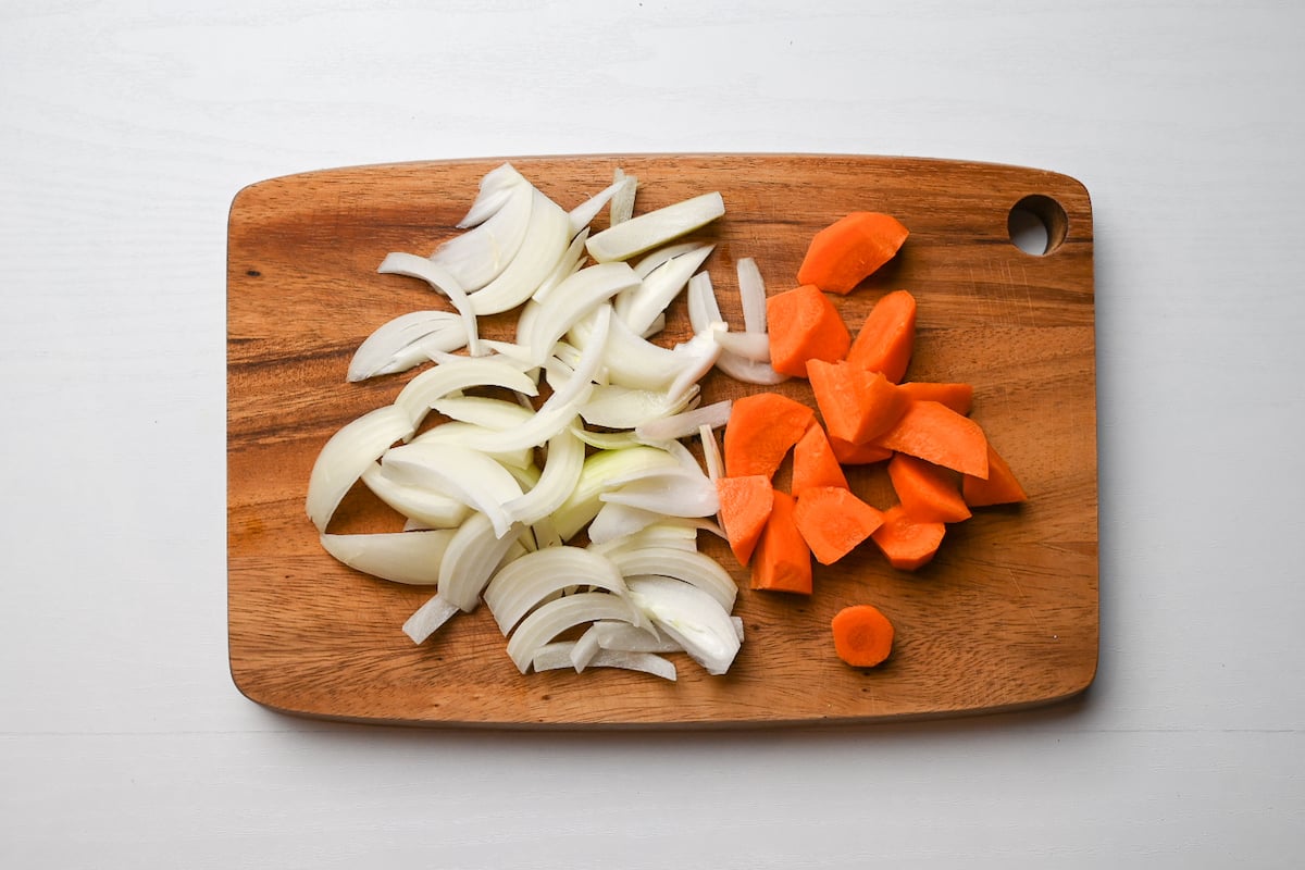 Nikujaga: cut onions and carrots on wooden chopping board