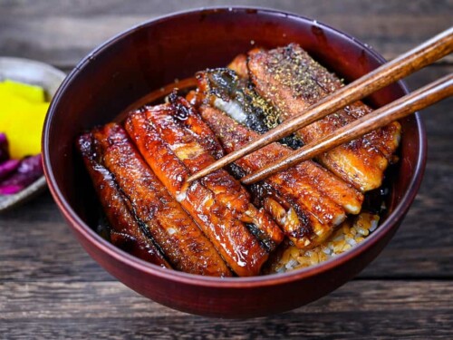Unagi don (Japanese Grilled Eel Rice Bowl) sprinkled with sansho Japanese pepper held with wooden chopsticks