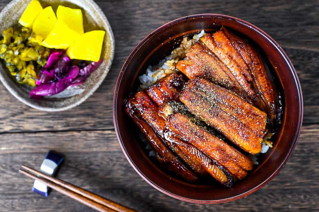 Unagi don (Japanese Grilled Eel Rice Bowl) sprinkled with sansho Japanese pepper with pickles top down