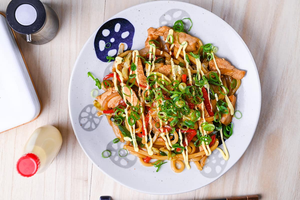 Chicken yaki udon served on a white plate, drizzled with Japanese mayo and topped with spring onions