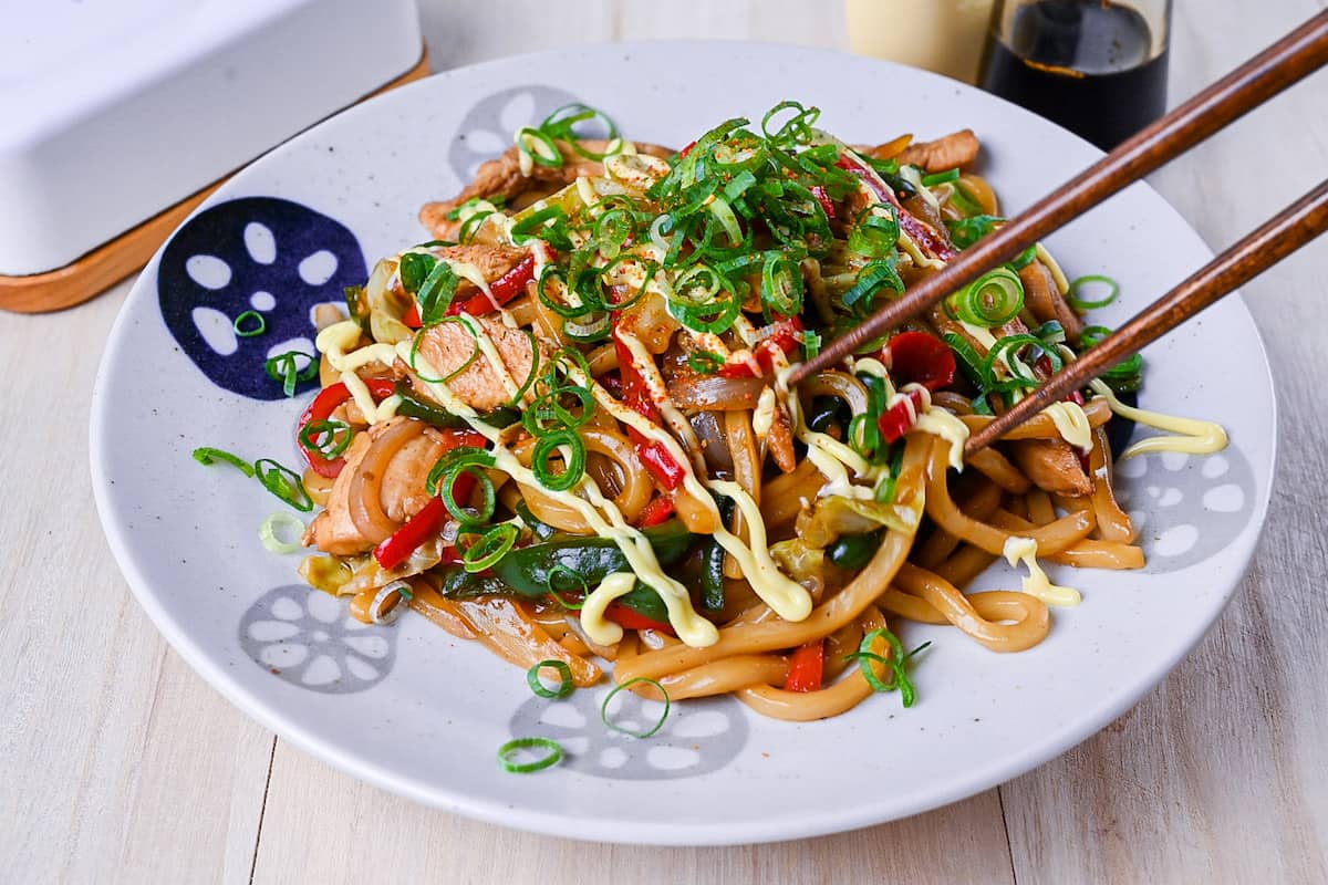 Chicken yaki udon served on a white plate, drizzled with Japanese mayo and topped with spring onions