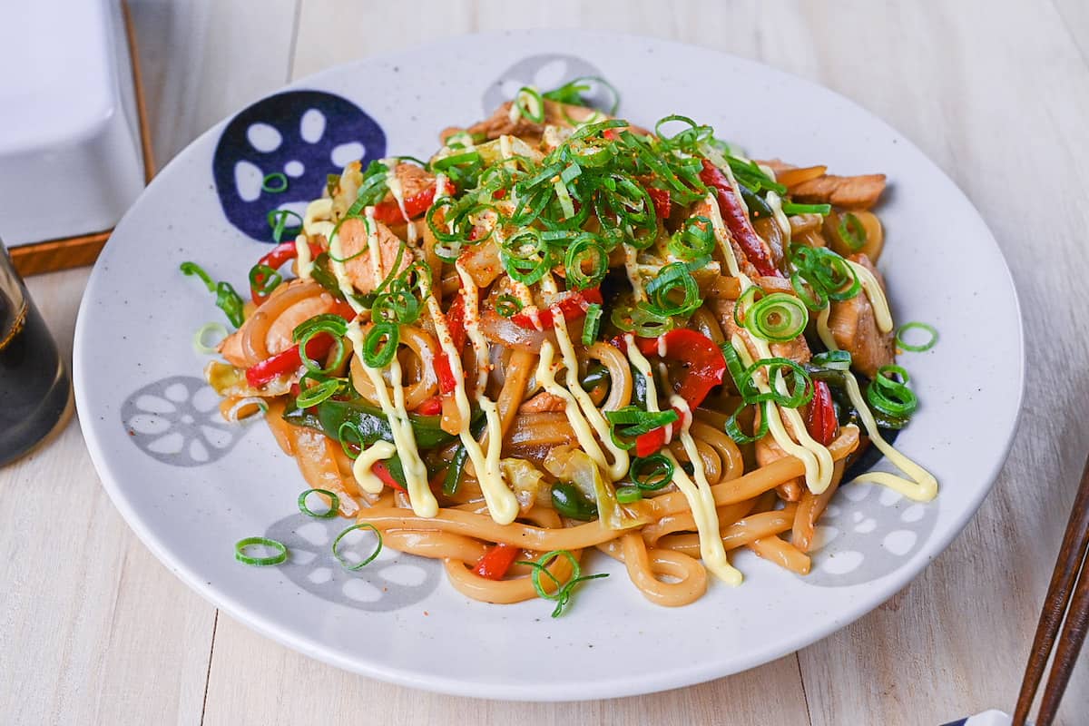 Chicken yaki udon served on a white plate, drizzled with Japanese mayo and topped with spring onions