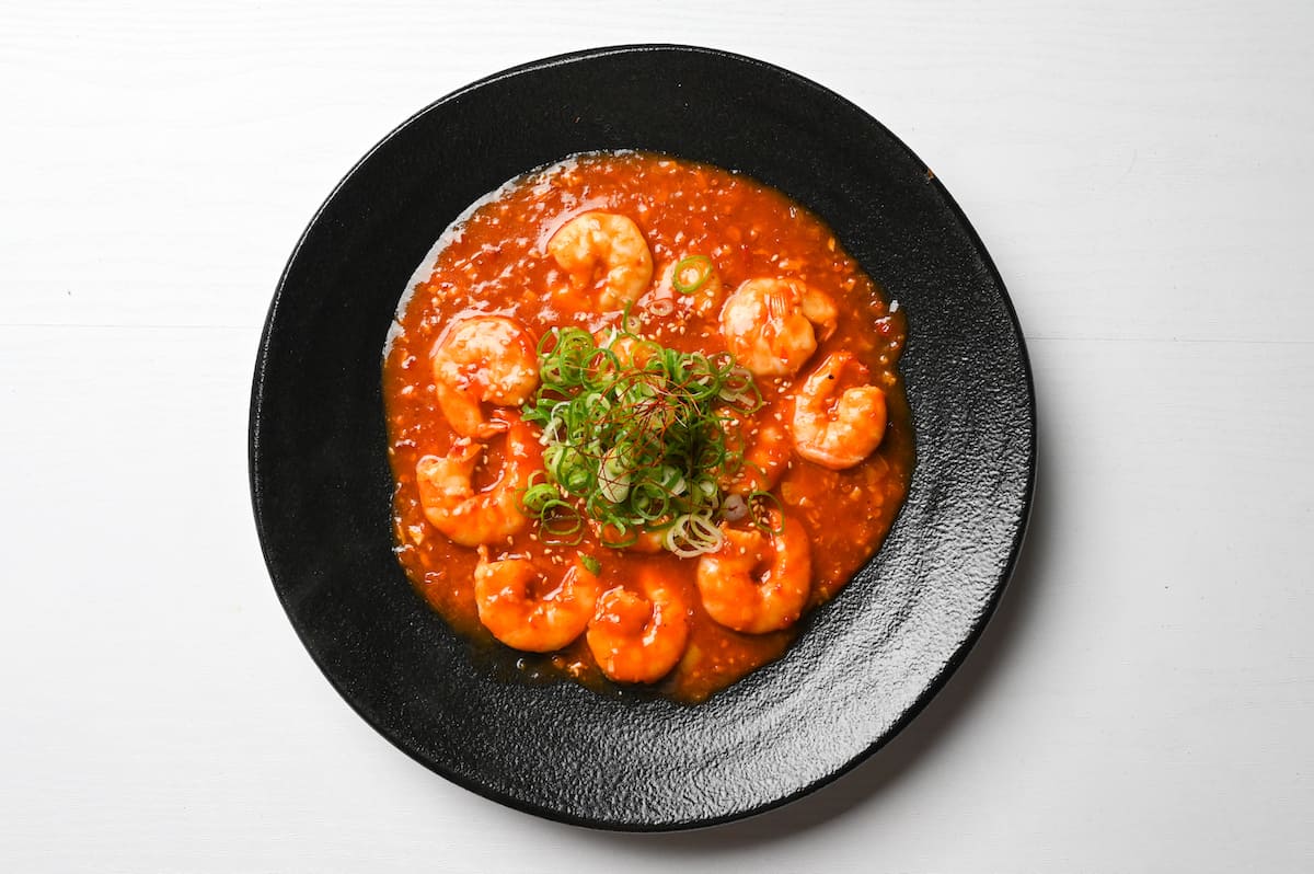 Ebi chili on a black plate with chopped spring onions and dried chili threads