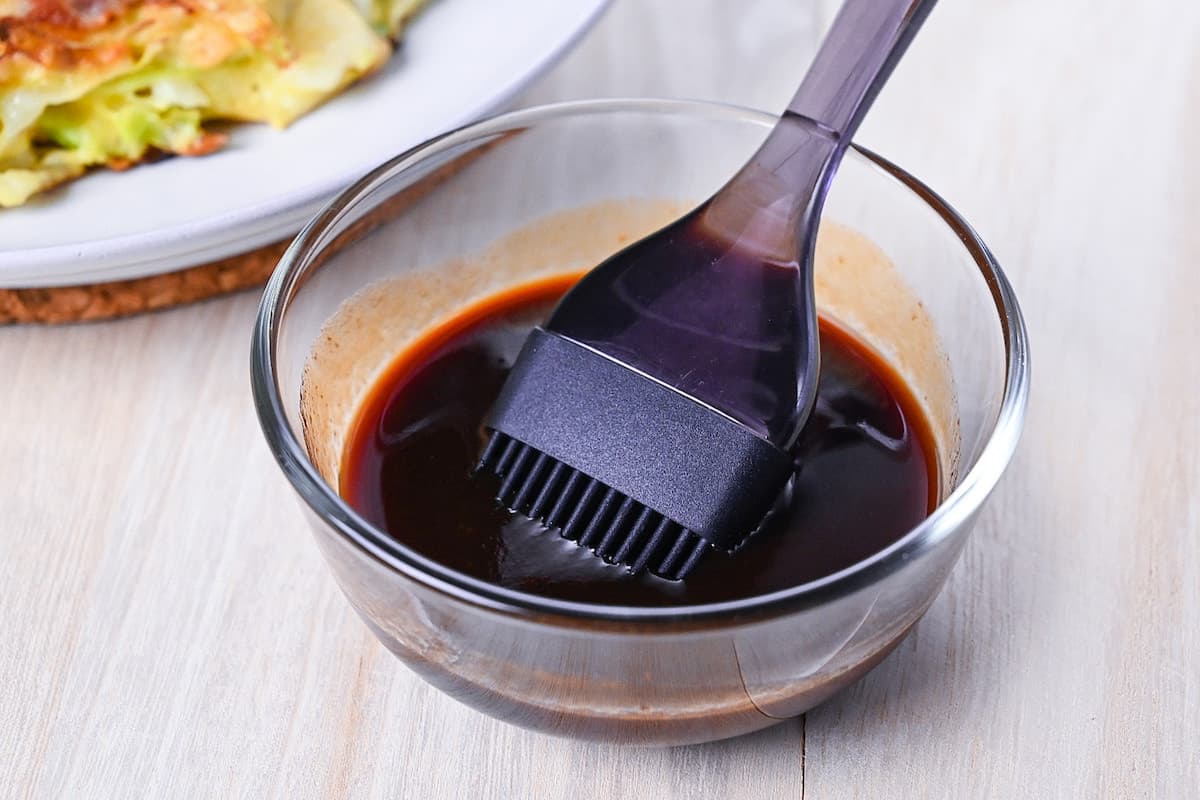 Homemade okonomiyaki sauce in a glass bowl with a silicone pastry brush