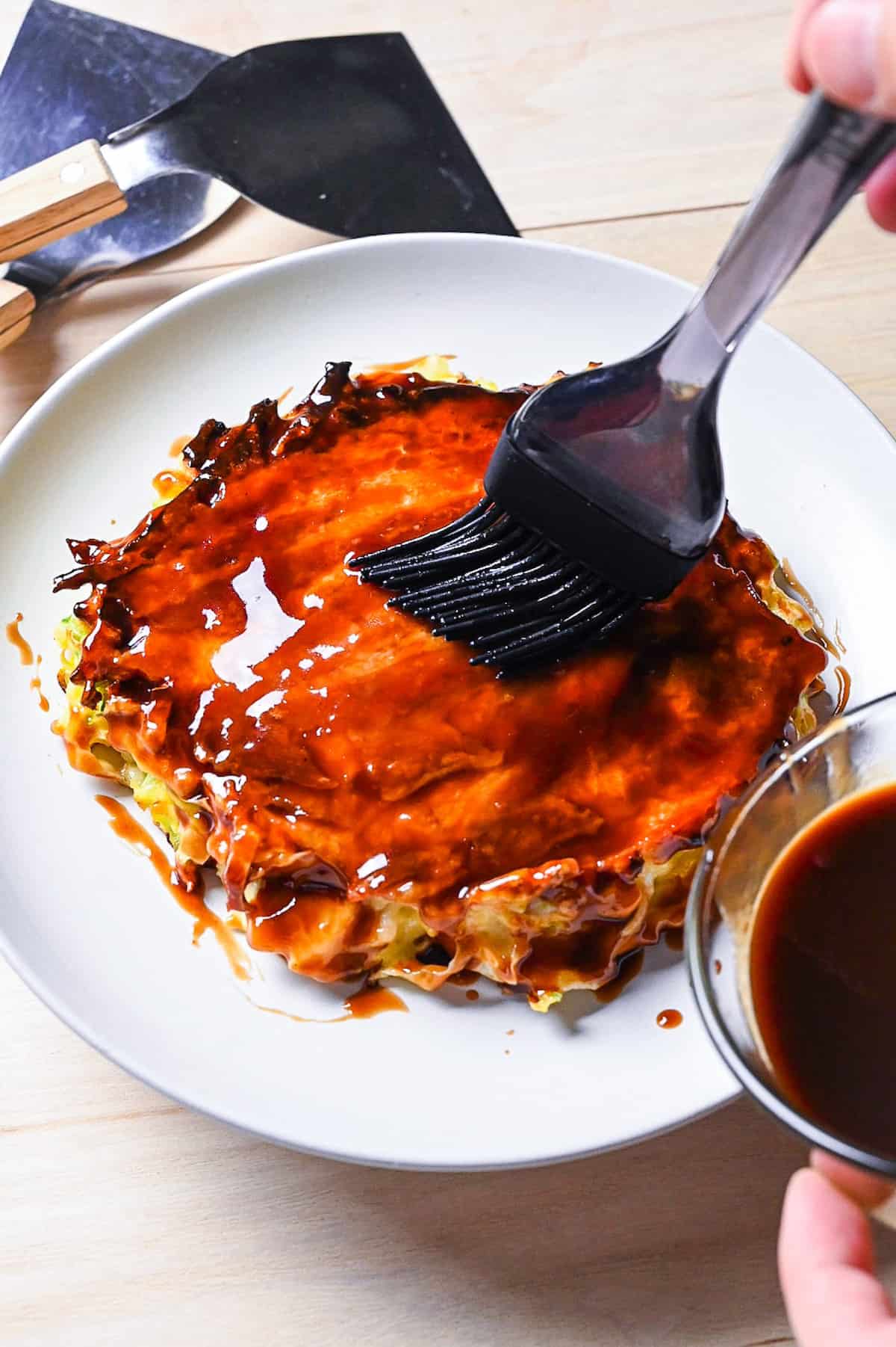 Homemade okonomiyaki sauce being brushed onto a freshly cooked okonomiyaki