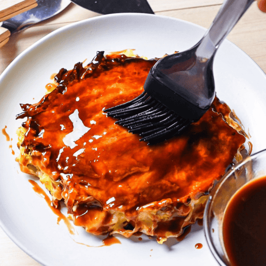 Homemade okonomiyaki sauce being brushed onto a freshly cooked okonomiyaki