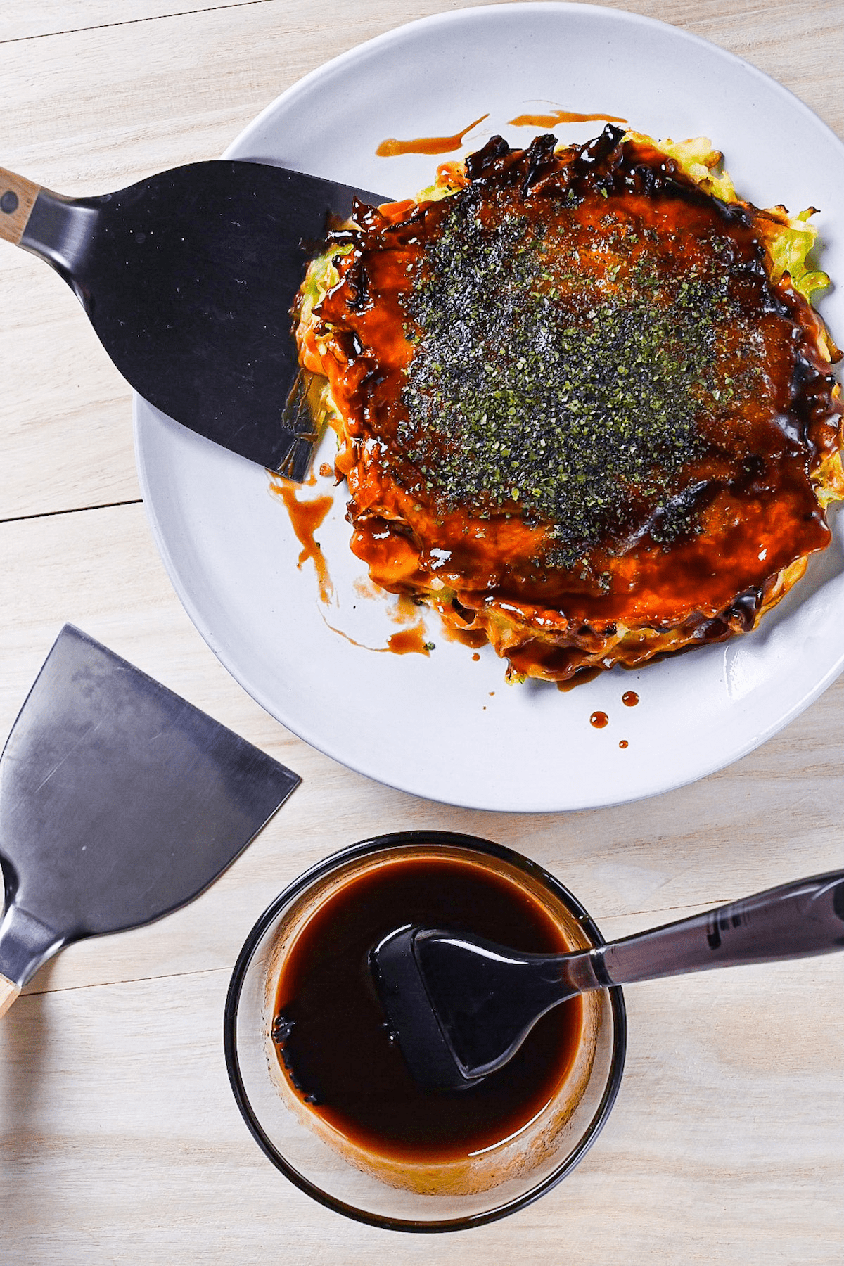 homemade okonomiyaki sauce in a glass bowl next to okonomiyaki on a white plate