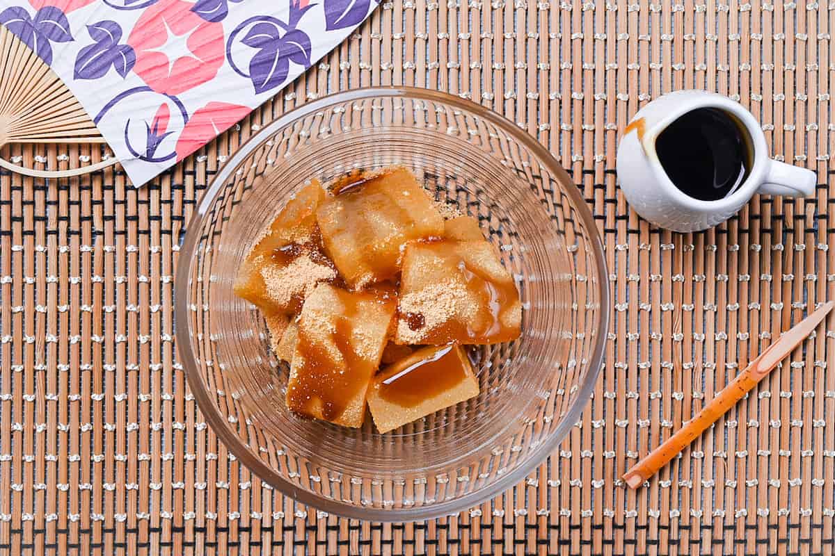 Homemade warabi mochi in a glass bowl coated with kinako and drizzled with kuromitsu syrup