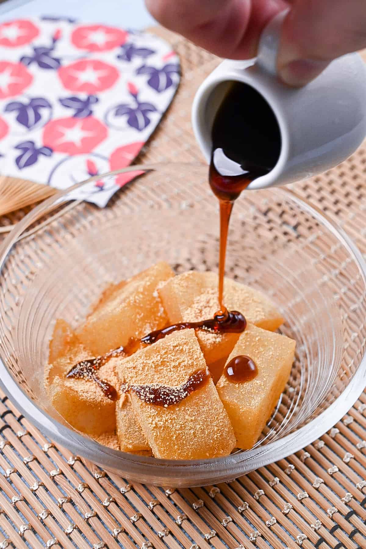 Homemade warabi mochi in a glass bowl coated with kinako and drizzled with kuromitsu syrup