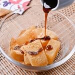 Homemade warabi mochi in a glass bowl coated with kinako and drizzled with kuromitsu syrup
