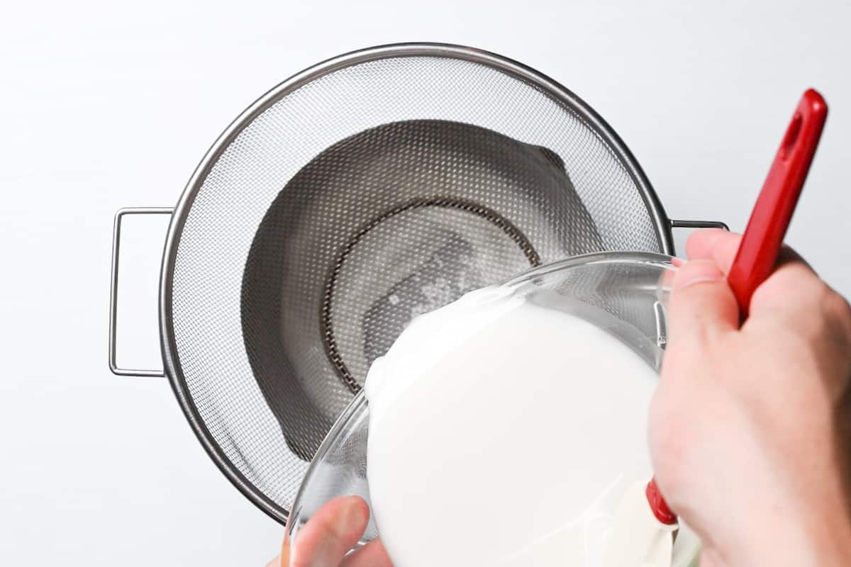 pouring warabi mochi mixture through a sieve into a saucepan