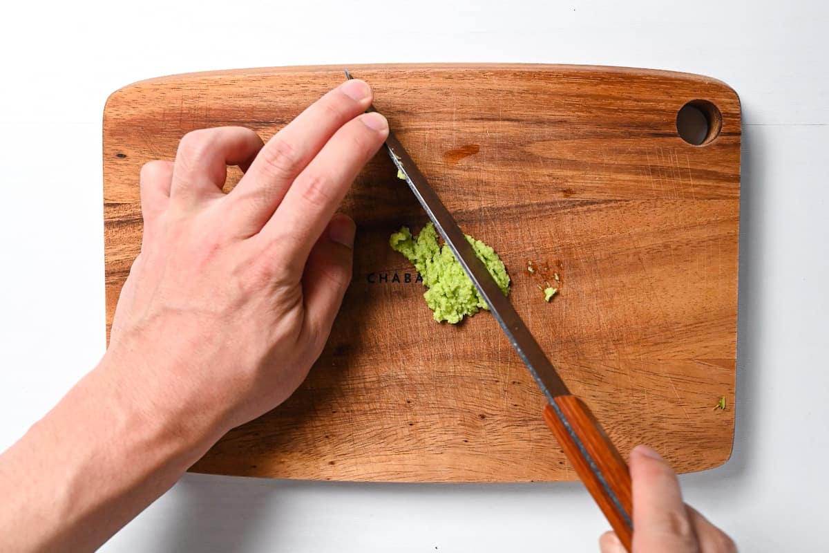 Wasabi paste being cut on a wooden chopping board
