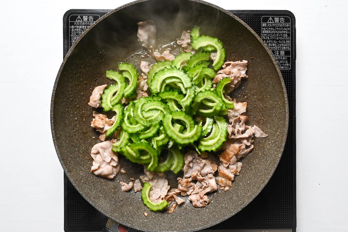 Thinly sliced pork belly and goya (Okinawan bitter melon) cooking in a frying pan