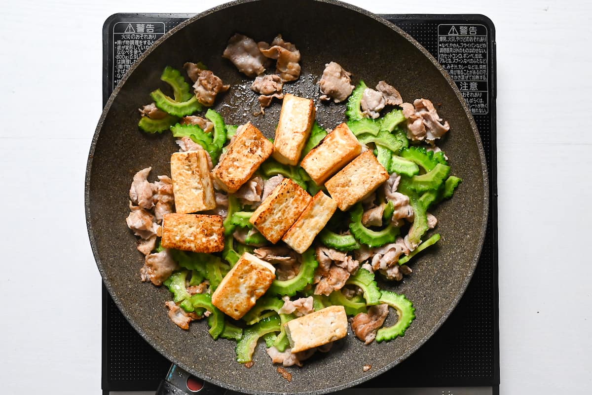 Thinly sliced pork belly, goya (Okinawan bitter melon) and firm tofu cooking in a frying pan