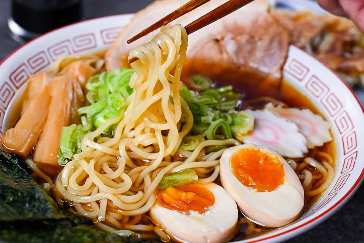 Homemade shoyu ramen topped with ramen egg, menma, narutomaki, chashu, chopped spring onions and nori in a white and red Chinese style noodle bowl