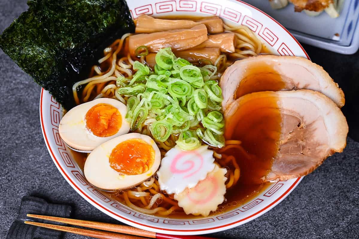 Homemade shoyu ramen topped with ramen egg, menma, narutomaki, chashu, chopped spring onions and nori in a white and red Chinese style noodle bowl