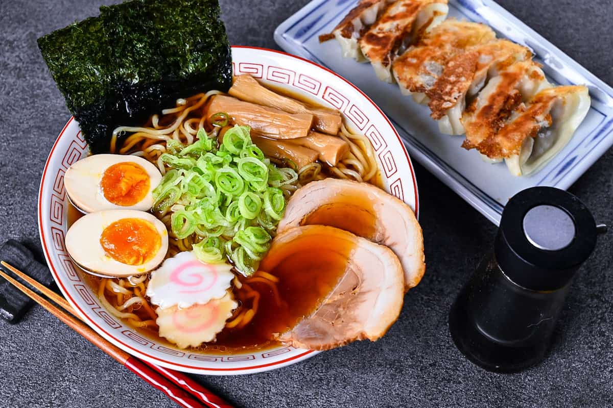 Homemade shoyu ramen topped with ramen egg, menma, narutomaki, chashu, chopped spring onions and nori in a white and red Chinese style noodle bowl