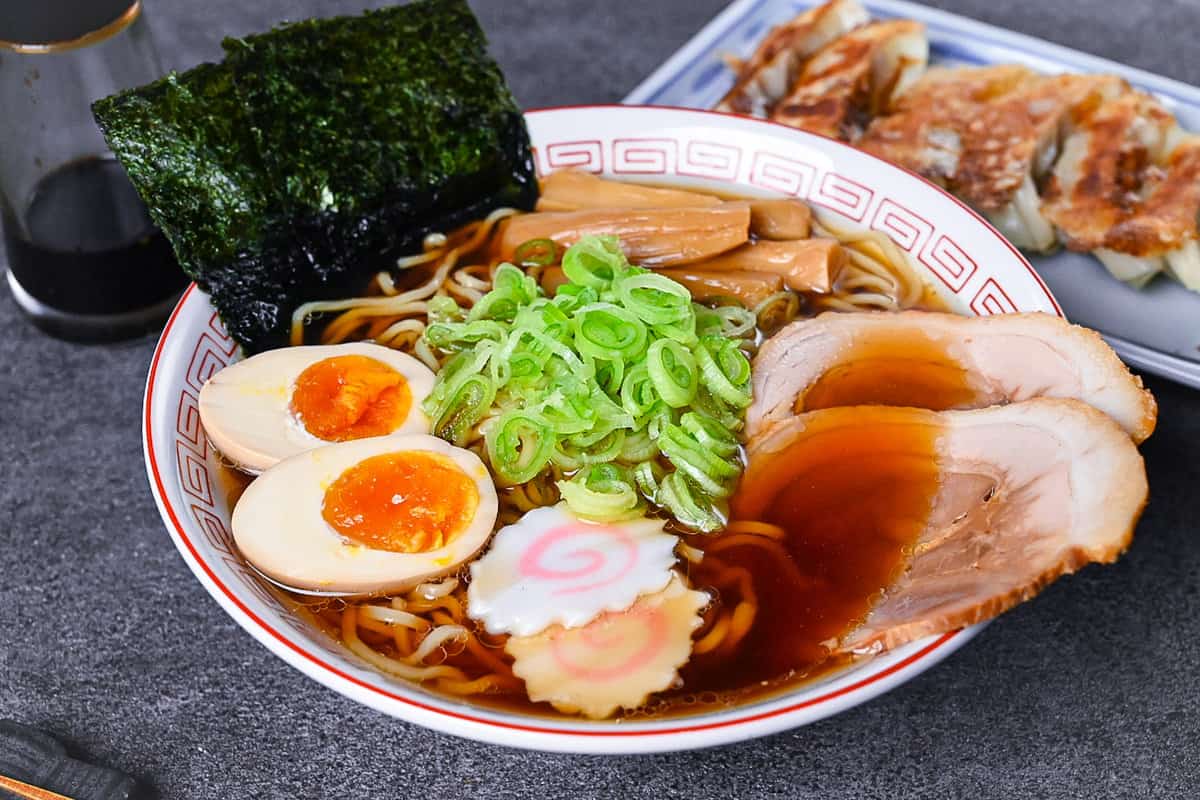 Homemade shoyu ramen topped with ramen egg, menma, narutomaki, chashu, chopped spring onions and nori in a white and red Chinese style noodle bowl