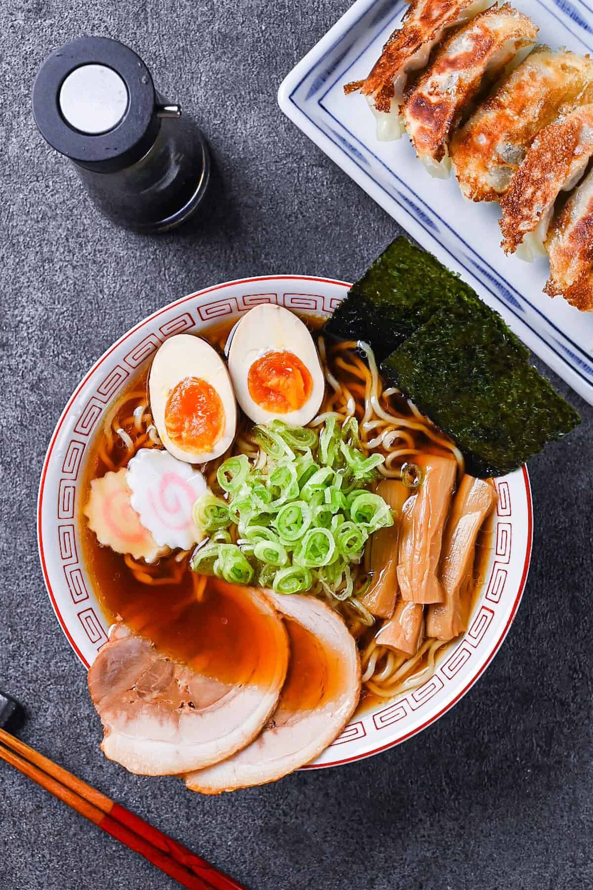 Homemade shoyu ramen topped with ramen egg, menma, narutomaki, chashu, chopped spring onions and nori in a white and red Chinese style noodle bowl