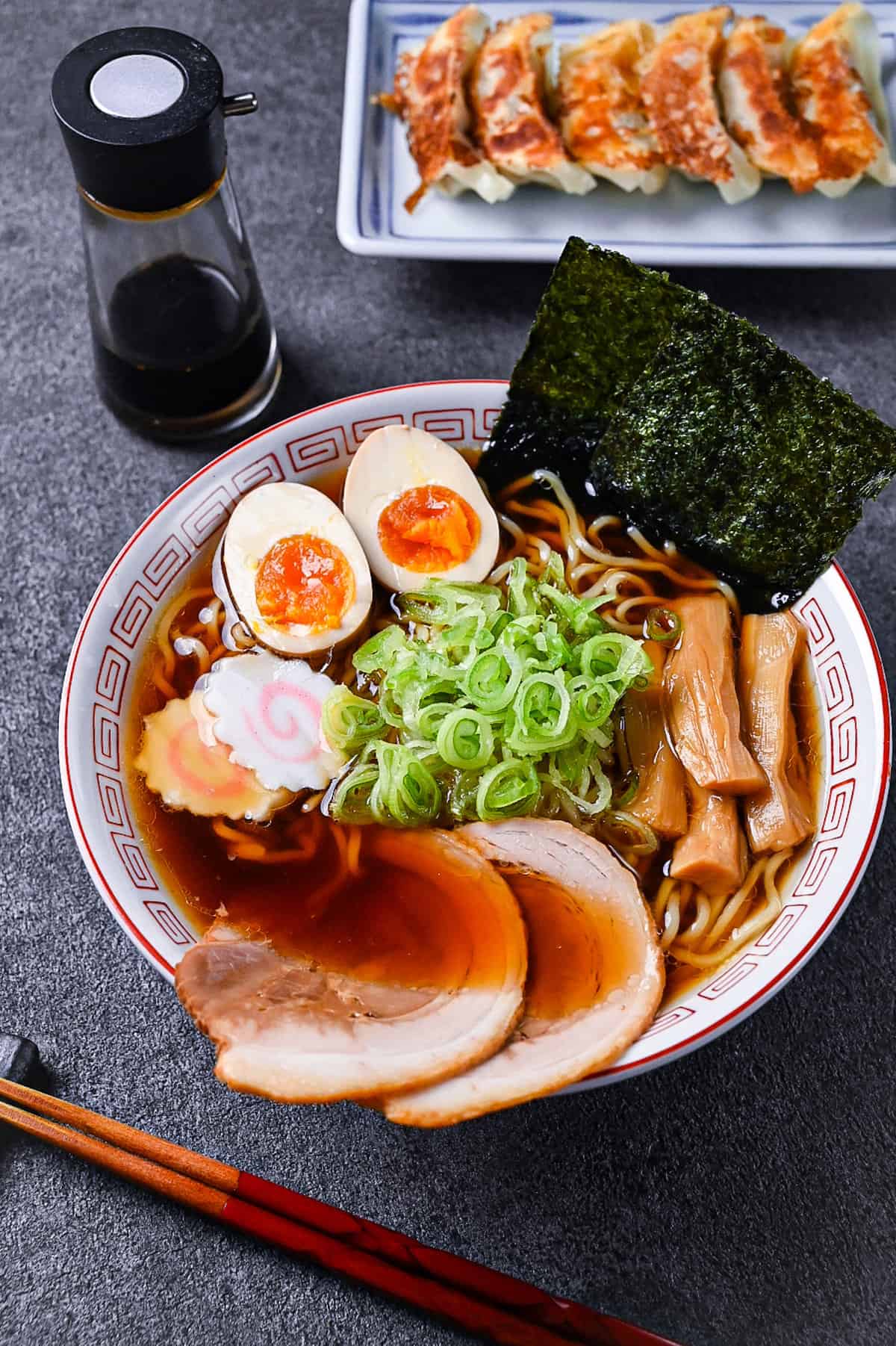 Homemade shoyu ramen topped with ramen egg, menma, narutomaki, chashu, chopped spring onions and nori in a white and red Chinese style noodle bowl