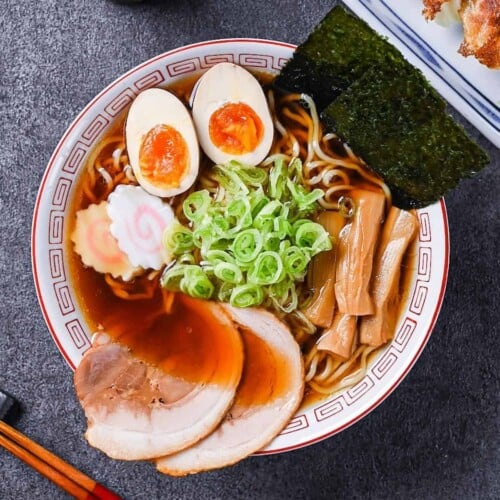 Homemade shoyu ramen topped with ramen egg, menma, narutomaki, chashu, chopped spring onions and nori in a white and red Chinese style noodle bowl
