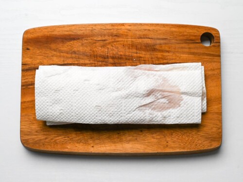 chicken breast wrapped in kitchen paper on a wooden chopping board