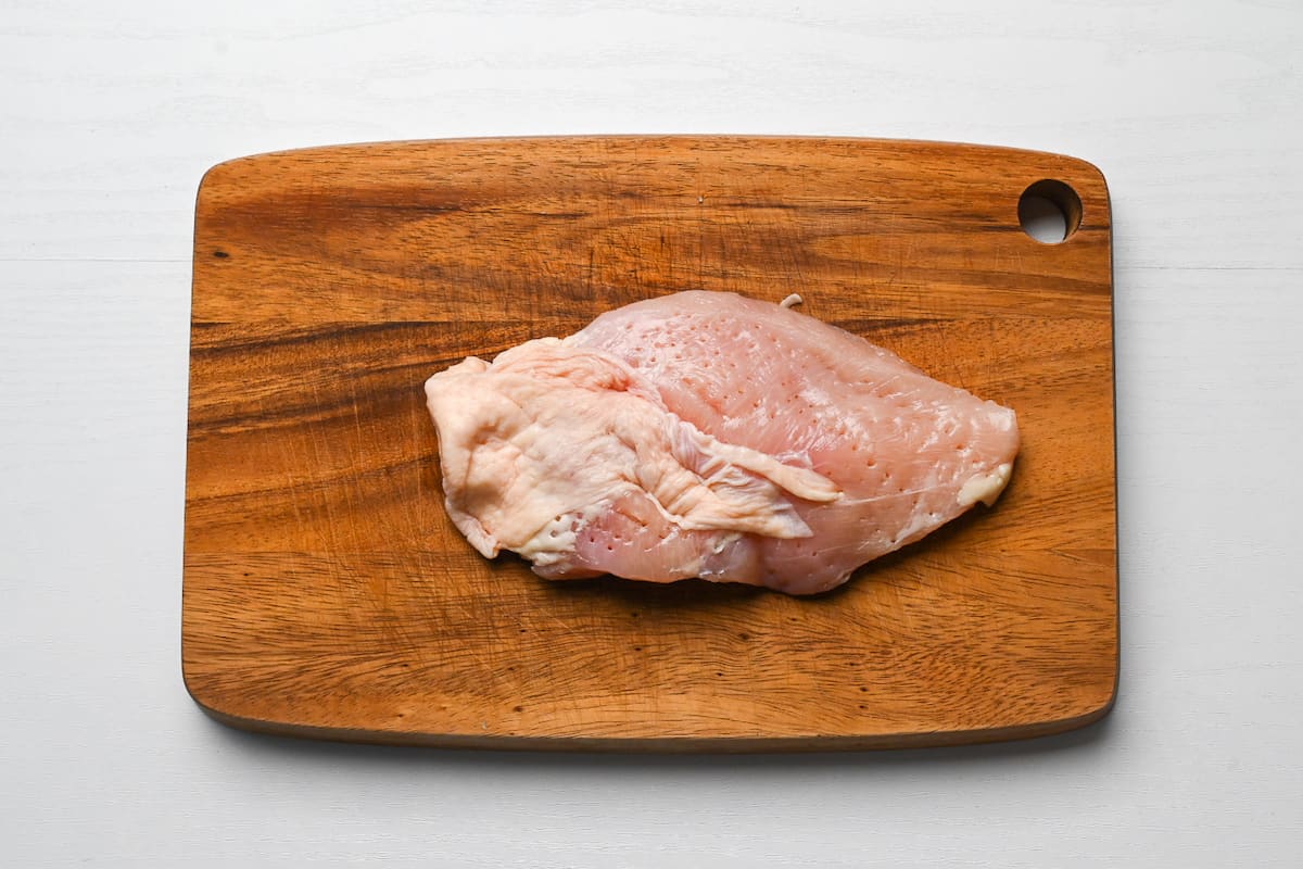 chicken breast pierced with a fork on a wooden chopping board