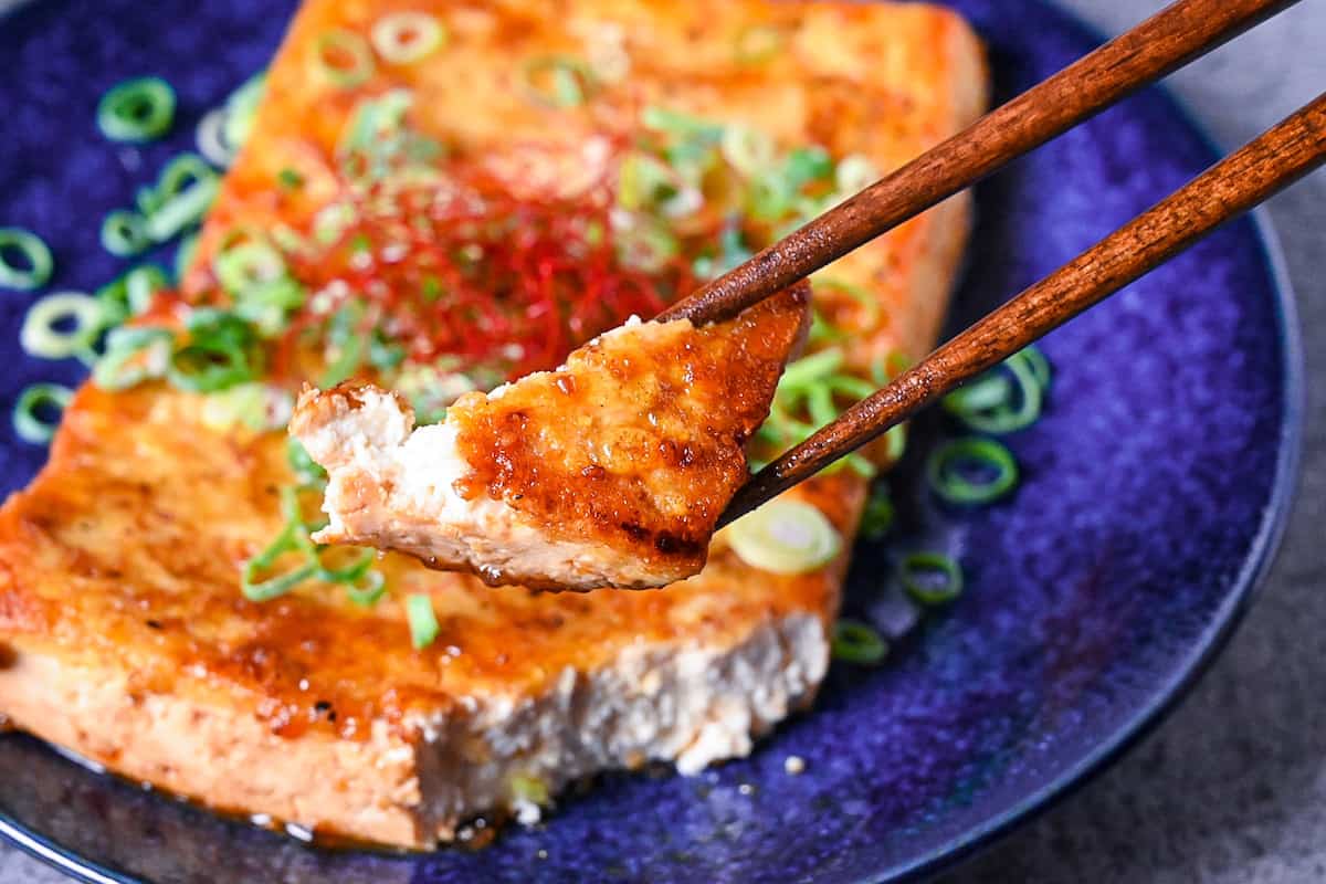 Tofu steak coated in a Japanese style sauce cut and picked up with wooden chopsticks
