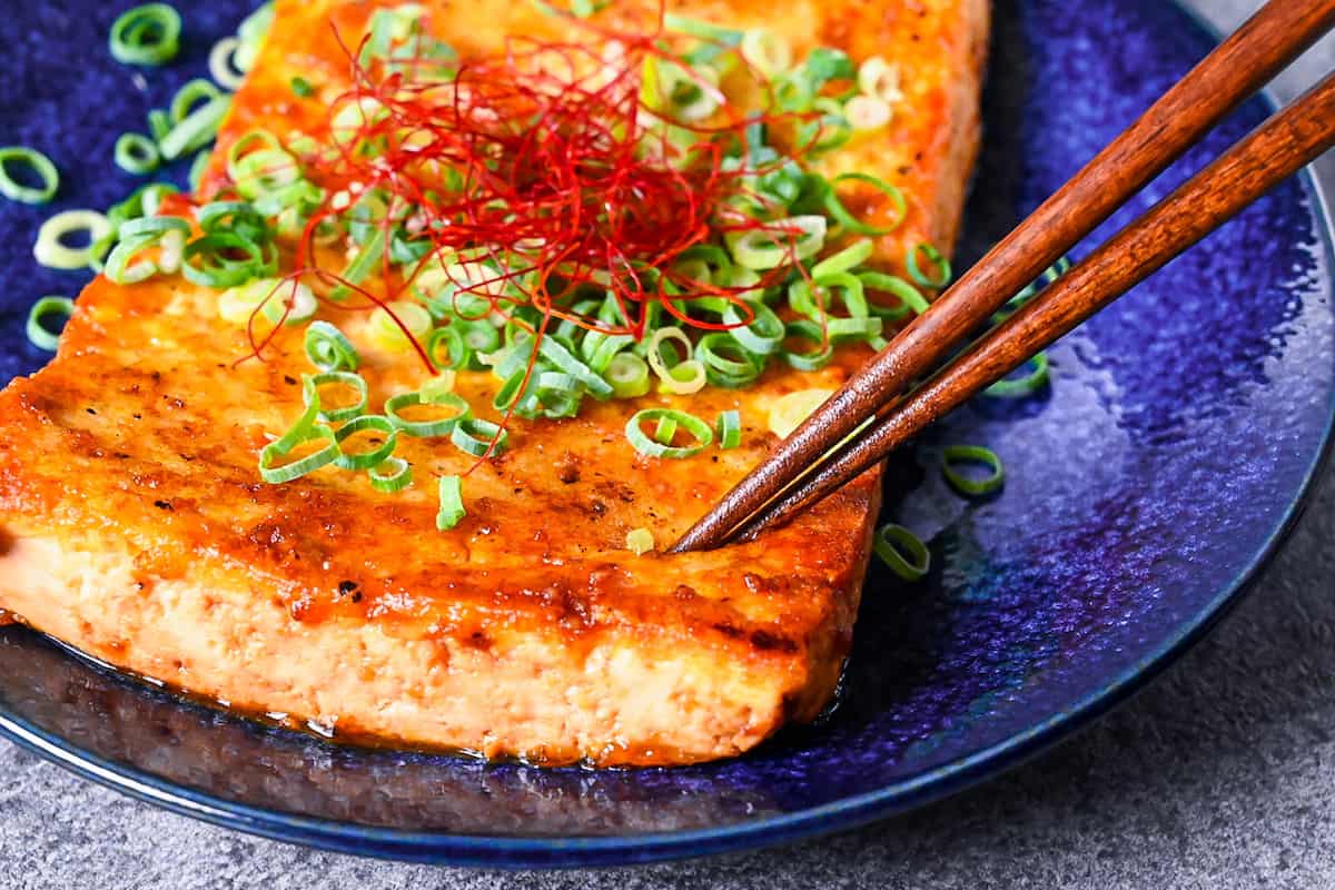 Japanese style tofu steak being cut with wooden chopsticks